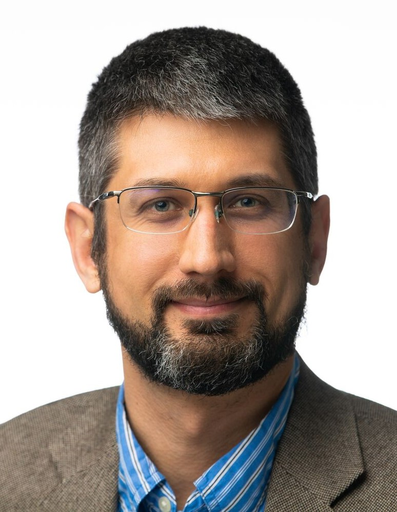 A professional portrait of Eric Wiedner, a middle aged man with short dark hair, white skin and brown eyes. 